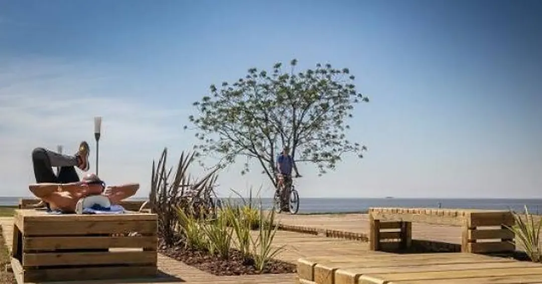 Paseo de la Costa de Vicente López: deck de madera sobre la ribera del Río de la Plata, con un árbol y el horizonte del río al fondo